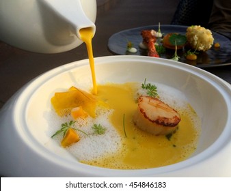 Pouring soup, Closeup of pumpkin soup into seared scallops and Parmesan foam in white plate with blur food dish background - Powered by Shutterstock