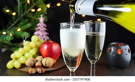 Pouring sparkling white wine in glasses on Christmas table. Christmas tree, lights and decorations in the background.