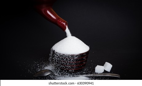 Pouring Sugar Into A Little Cup In Front Of Black Background - Concept Of Sugary Drinks