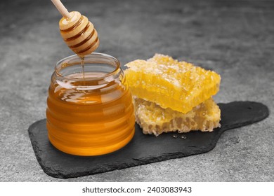 Pouring sweet golden honey from dipper into jar and pieces of honeycomb on grey textured table - Powered by Shutterstock