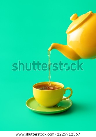 Pouring tea from a ceramic teapot in a cup, minimalist on a green table. Hot mint tea in a yellow colored cup isolated on a green background