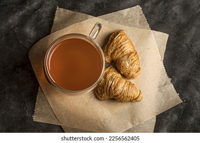 Pouring tea into cup of tea. breakfast on a dark background. tea ceremony and croissant with cream. - Shutterstock ID 2256562405