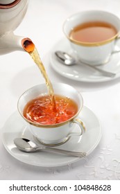 Pouring Tea From The Tea Pot Into The Cups Isolated On White Background