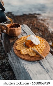 Pouring tea from a thermos and having a waffle with cloudberries outdoor on a log