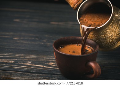 Pouring turkish coffee into vintage cup on wooden background