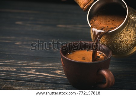 Pouring turkish coffee into vintage cup on wooden background