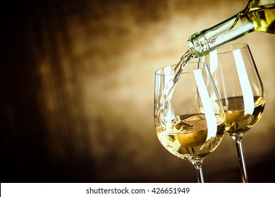 Pouring two glasses of white wine from a bottle in a close up view of the wineglasses over an abstract brown blue background with copy space - Shutterstock ID 426651949