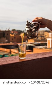 Pouring Typical Morrocan Fresh Mint Tea From A Silver Karraffe Into A Tea Glass Above The Roofs Of The Medina Of Marrakesh (Marrakesh, Morocco, Africa)