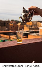 Pouring Typical Morrocan Fresh Mint Tea From A Silver Karraffe Into A Tea Glass Above The Roofs Of The Medina Of Marrakesh (Marrakesh, Morocco, Africa)