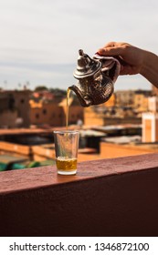 Pouring Typical Morrocan Fresh Mint Tea From A Silver Karraffe Into A Tea Glass Above The Roofs Of The Medina Of Marrakesh (Marrakesh, Morocco, Africa)