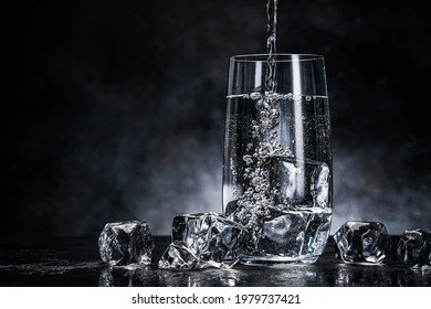 Pouring Water From Bottle Into Glass With Ice Cubes On Black Background