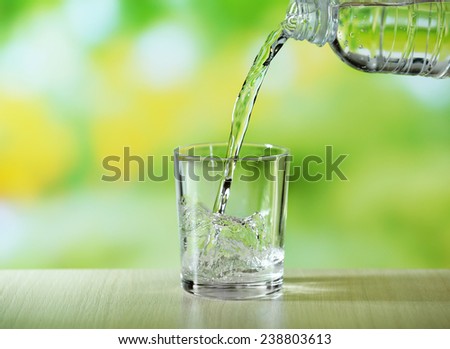 Pouring water from bottle on  glass on bright background