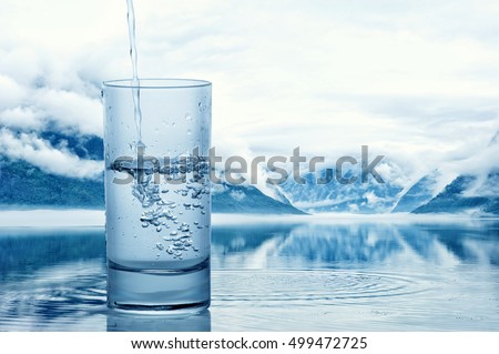 Pouring water into a glass against the nature landscape