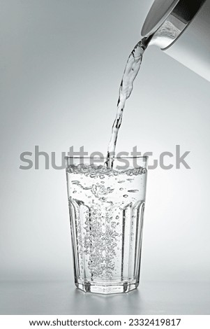 Pouring water into a glass on grey background, close-up