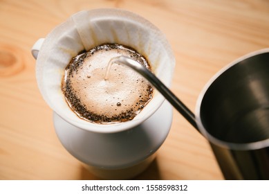 Pouring Water From The Kettle Into The Coffee Filter. Pour Over Coffee Blossoms In The Dripper. Brewing Coffee Alternative Method In Pour Over, Top View On Wood Table