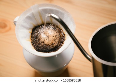 Pouring water from the kettle into the coffee filter. Pour over coffee blossoms in the dripper. Brewing coffee alternative method in pour over, top view on wood table - Shutterstock ID 1558598318