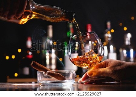 Pouring a whiskey in a glass on bar counter, smoking cigar