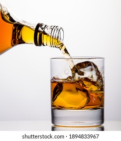 Pouring Whisky From A Bottle Into A Tumbler On White Background