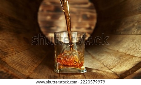 Pouring whisky into glass inside old wooden barrel. Concept of fresh beverages.