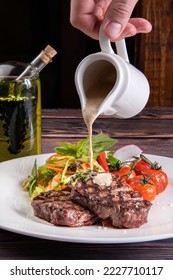 Pouring white cream sauce over juicy piece of meat. The chef's hand decorating the food pours sauce over the steak
