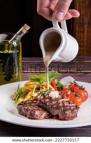 Pouring white cream sauce over juicy piece of meat. The chef's hand decorating the food pours sauce over the steak