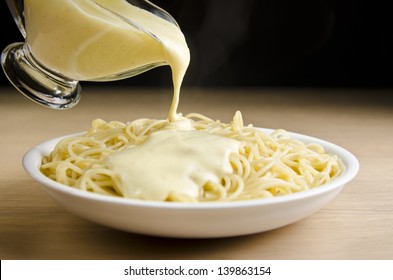 Pouring White Sauce Over Plate Of Cooked Spaghetti