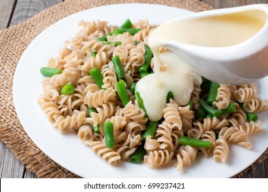 Pouring White Sauce Over Plate Of Cooked Pasta