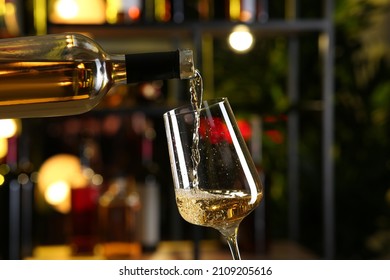 Pouring white wine from bottle into glass on blurred background, closeup