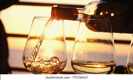 Pouring white wine in glasses at amazing sunset by the sea in beach cafe.