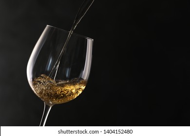 Pouring white wine into glass on dark background. Space for text