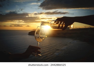 Pouring white wine into the glass against a breathtaking seaside sunset. - Powered by Shutterstock