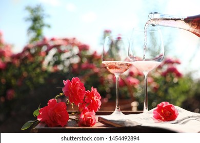 Pouring Wine Into Glass On Table In Blooming Rose Garden. Space For Text