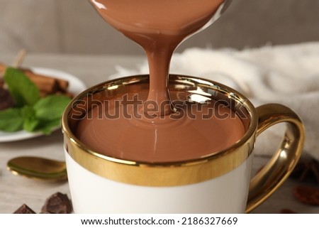 Pouring yummy hot chocolate into cup on table, closeup