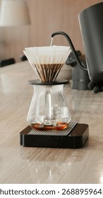 Pour-over coffee with sharp focus and soft lighting focused on the process of hot water dripping from a black gooseneck kettle onto coffee grounds in a cone dripper.