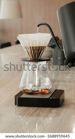 Pour-over coffee with sharp focus and soft lighting focused on the process of hot water dripping from a black gooseneck kettle onto coffee grounds in a cone dripper.