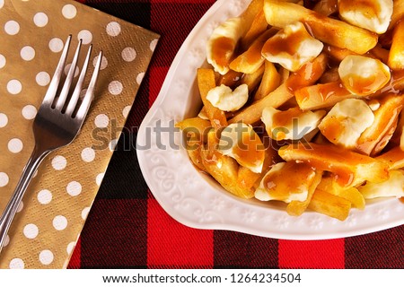 Poutine plate on a red and black tartan tablecloth. Meal cooked with french fries, beef gravy and curd cheese. Canadian cuisine.