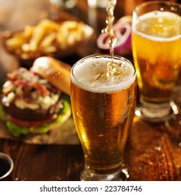 pouting beer into glass with burgers on wooden table top