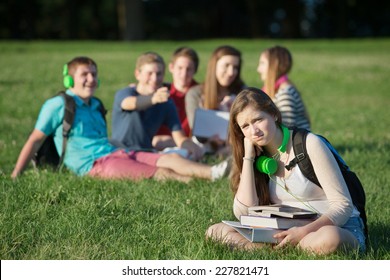 Pouting Teen Girl Near Group On Grass Outdoors