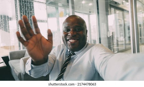 Pov of African American businessman in formal clothes chatting to family on smartphone and waving his hand happily in a classy cafe. He gesticulates actively and cheerfully.