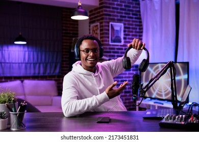 POV of african american vlogger doing product review on camera, recording headphones recommendation in studio. Male influencer talking about wireless headset to film live broadcast.