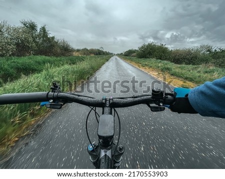 POV of cycling during heavy rain. A man holds handlebar with one hand during pouring rainfall