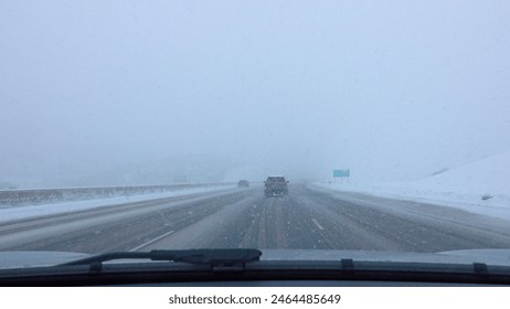 POV: Driving down the interstate freeway in Utah during severe snowstorm. Commuters carefully drive along the slippery snow and ice covered motorway leading to Salt Lake City. Driving through blizzard