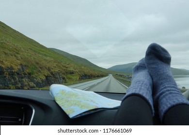 POV: Driving Down Scenic Coastal Road With Your Feet Resting On The Dashboard In Cozy Woolen Socks. Cool Shot Of Unrecognizable Woman's Legs On The Car Dashboard As She Drives Down The Empty Road.