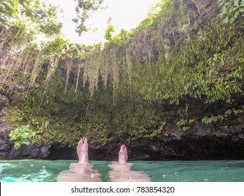 POV Of Female Feet With Nail Polish Floating In To Sua Trench Swimming Hole, Upolu Island, Western Samoa, South Pacific. Lush Greenery Growing On Side Of Cave.