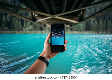 POV Of Hand Holding Smartphone And Making Photo Of Turquoise Lake And Bridge Metal Construction For Share On Social Media Channels, Concept Millennial Nomads 