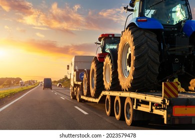 POV heavy industrial truck semi trailer flatbed platform transport two big modern farming tractor machine on common highway road at sunset sunrise sky. Agricultural equipment transportation service - Shutterstock ID 2023579478
