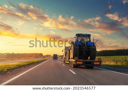 POV heavy industrial truck semi trailer flatbed platform transport two big modern farming tractor machine on common highway road at sunset sunrise sky. Agricultural equipment transportation service