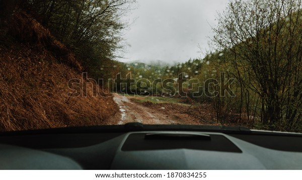 POV inside car windshield view point. Driver\
driving a modern off road left hand drive LHD car on the mountain\
forest dirty country road. Face reflecting in inside mirror.Safely\
auto driving concept
