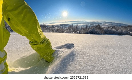 POV, LENS FLARE: Snowboarder makes tracks in freshly fallen snow as he descends the slope with a picturesque view of white valley. Snowflakes spray and glisten in the morning light while snowboarding.