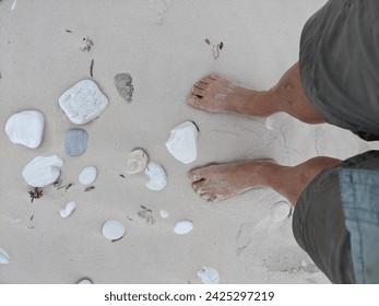 POV looking down to bare feet on white sandy beach with bleached stones